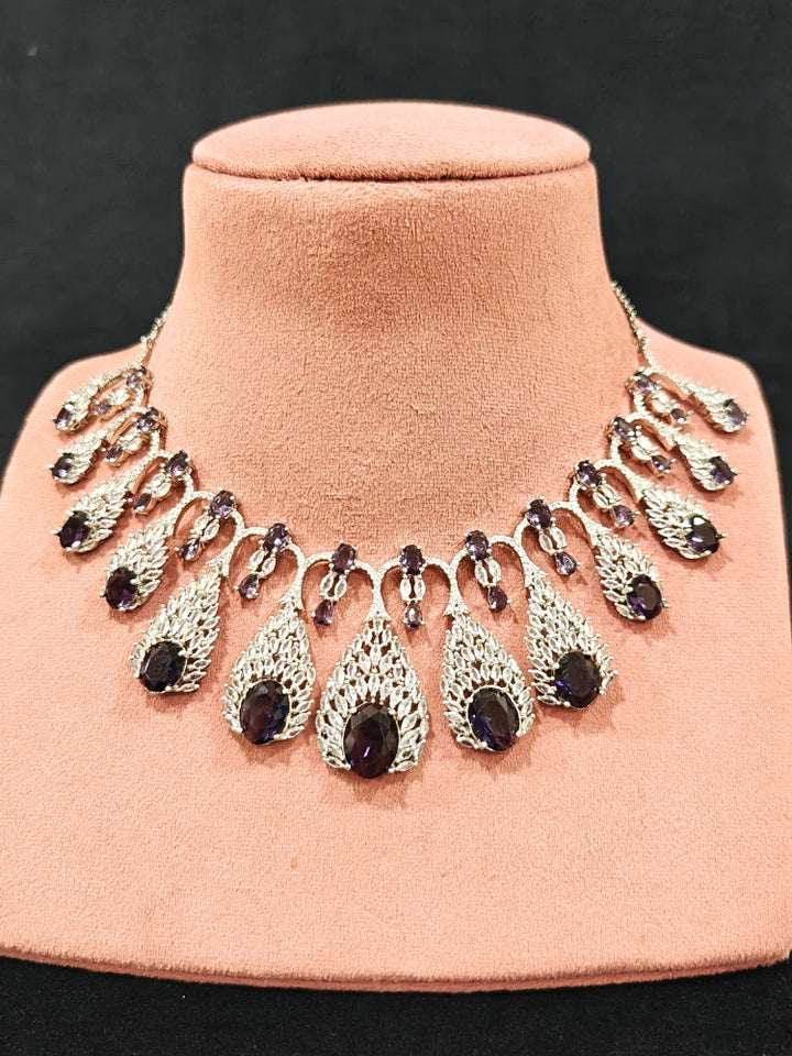 Close-up of an ornate Western Purple Diamond Silver Collar jewellery set and earrings with American Diamond and Purple Colored Stones. A luxury American diamond necklace set styled beautifully for a wedding guest look in India. Elegant wedding jewelry look featuring a premium artificial American diamond necklace.