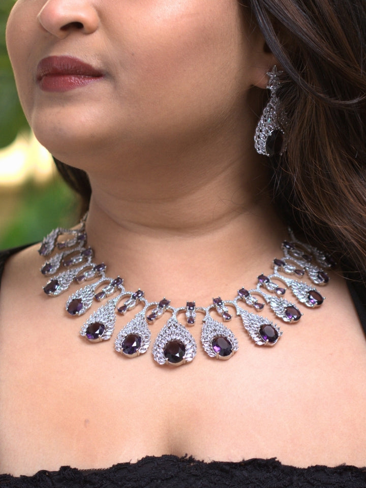 Close-up of a woman wearing an ornate Western Purple Diamond Silver Collar jewellery set and earrings with American Diamond and Purple Colored Stones. A woman wearing a luxury American diamond necklace set styled beautifully for a wedding guest look in India. Elegant wedding jewelry look featuring a premium artificial American diamond necklace.