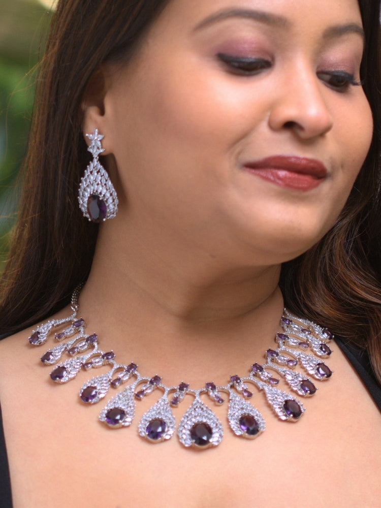Close-up of a woman wearing an ornate Western Purple Diamond Silver Collar jewellery set and earrings with American Diamond and Purple Colored Stones. A woman wearing a luxury American diamond necklace set styled beautifully for a wedding guest look in India. Elegant wedding jewelry look featuring a premium artificial American diamond necklace.