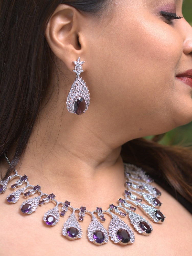 Close-up of a woman wearing an ornate Western Purple Diamond Silver Collar jewellery set and earrings with American Diamond and Purple Colored Stones. A woman wearing a luxury American diamond necklace set styled beautifully for a wedding guest look in India. Elegant wedding jewelry look featuring a premium artificial American diamond necklace.