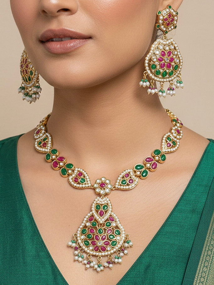 Close-up of a woman wearing an ornate traditional Collar jadau gold jewellery set and jadau earrings with Pearl and Pink and Green gemstones. Close-up of a luxury Jadau imitation necklace styled with a Anarkali. Elegant reception look featuring a luxury Jadau artificial jewelry set.
