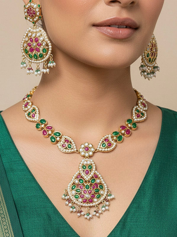 Close-up of a woman wearing an ornate traditional Collar jadau gold jewellery set and jadau earrings with Pearl and Pink and Green gemstones. Close-up of a luxury Jadau imitation necklace styled with a Anarkali. Elegant reception look featuring a luxury Jadau artificial jewelry set.