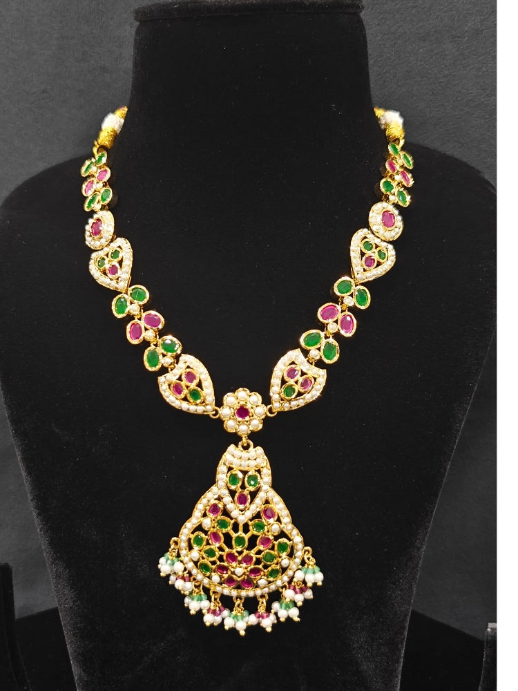 Close-up of an ornate traditional Collar jadau gold jewellery set and jadau earrings with Pearl and Pink and Green gemstones. Festive saree look completed with a handcrafted Jadau necklace.
Festive celebration look featuring a Jadau artificial necklace.