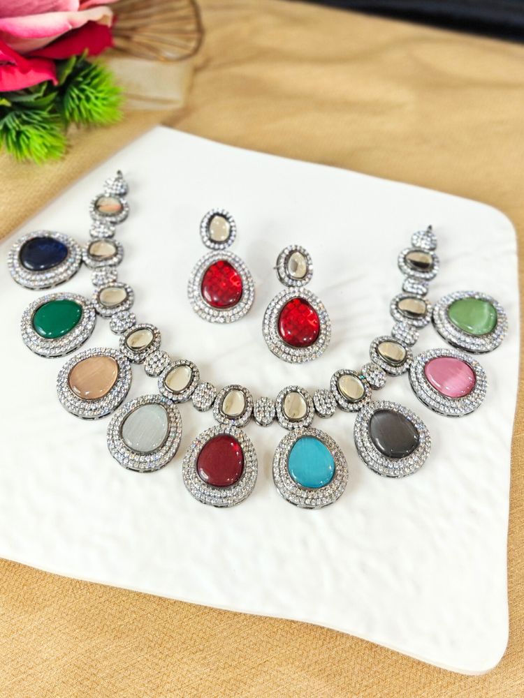 A woman with brown hair down smiles to the side, wearing the Multi-Color Elizabeth Necklace Set featuring a statement Victorian-style necklace and matching earrings with large colorful stones, paired with a sparkly dark top.