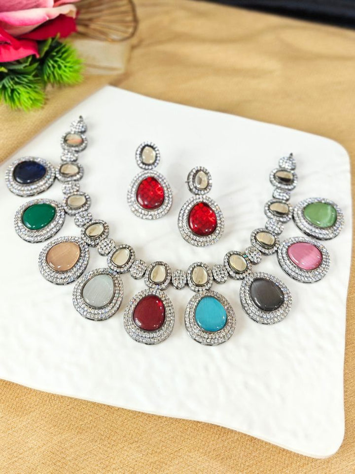A woman with brown hair down smiles to the side, wearing the Multi-Color Elizabeth Necklace Set featuring a statement Victorian-style necklace and matching earrings with large colorful stones, paired with a sparkly dark top.