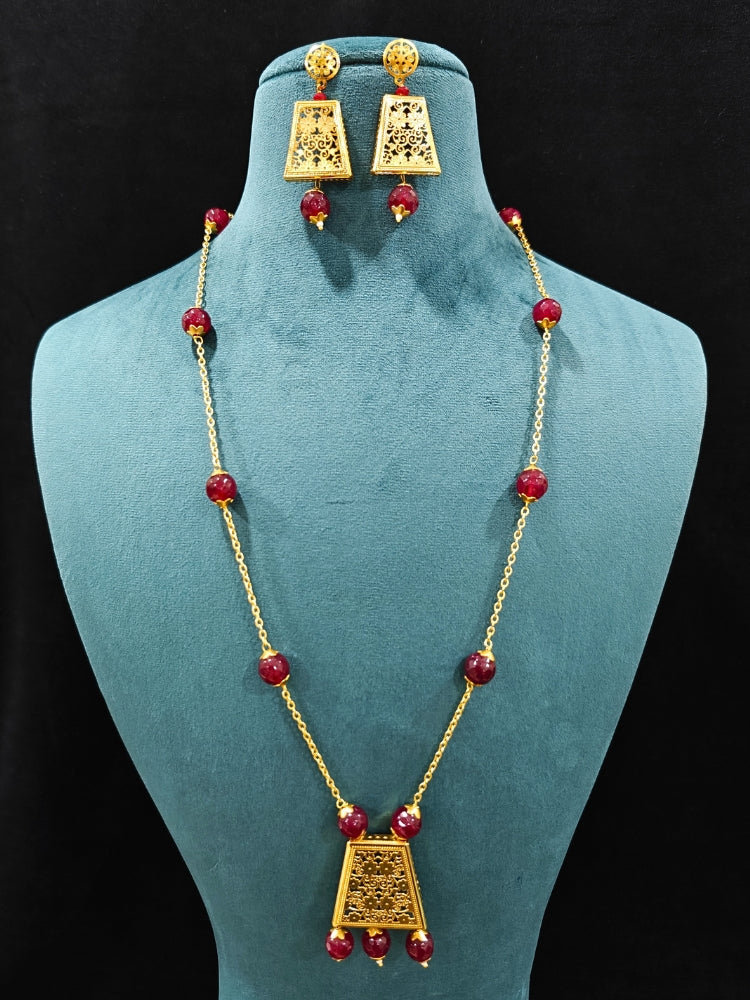 Close-up of an ornate traditional (Gold Polish) Long jewellery set and earrings with Filigree work and Red Colored Beads. Mehendi ceremony look completed with a handcrafted jewelry set. Festive Diwali outfit paired with a colorful  necklace.