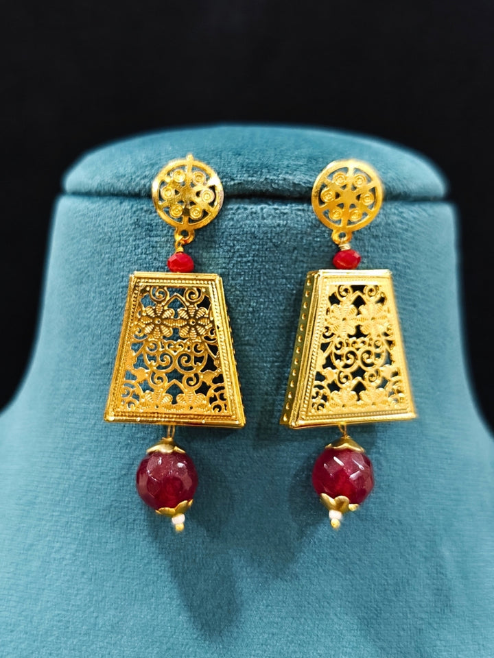 Close-up of an ornate traditional (Gold Polish) Long jewellery set and earrings with Filigree work and Red Colored Beads. Mehendi ceremony look completed with a handcrafted jewelry set. Festive Diwali outfit paired with a colorful  necklace.