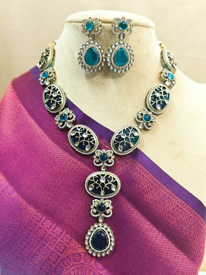 A mannequin draped in a pink and purple sari showcases the Namrita Teel Blue Necklace Set, featuring Monalisa stones with intricate Kundan detailing and ornate gold filigree work on top - made in mehendi polish. Comes with matching earrings. 
