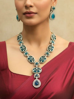 Close-up of a woman wearing an ornate traditional (Mehendi Gold Antique Finish) Teel blue long Colored Stone jewellery set and earrings with Kundan, Monalisa Stone and American Diamonds. Close-up of a premium imitation Colored Stones jewelry set styled with a bridal saree. Woman wearing trending Colored Stones artificial jewelry for wedding season in India.