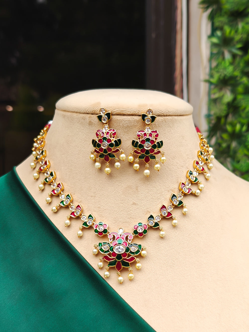 Close-up of an ornate traditional Red & Green Meenakari gold Collar jewellery set and earrings with American Diamond, Pearls and Meenakari.   Festive celebration look enhanced with traditional Meenakari jewelry. Close-up of detailed enamel craftsmanship in Meenakari jewelry.