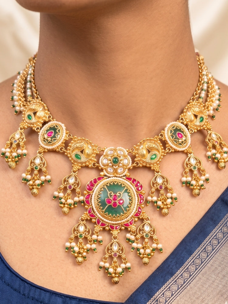 Close-up of a woman wearing an ornate traditional Mint Green Heritage gold Collar jewellery set and earrings with Pearls and Colored Stone. Saree styling inspiration with a traditional heritage necklace. Close-up of intricate antique finishing in heritage imitation jewelry.