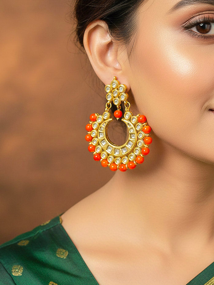 Close-up of a woman wearing an ornate traditional (Gold Polish) Orange Kundan Chandbali Long Earrings with Orange Colored Beads and Kundan. Woman wearing statement artificial Kundan earrings for a wedding guest look in India. Festive Diwali look styled with premium artificial Kundan earrings.