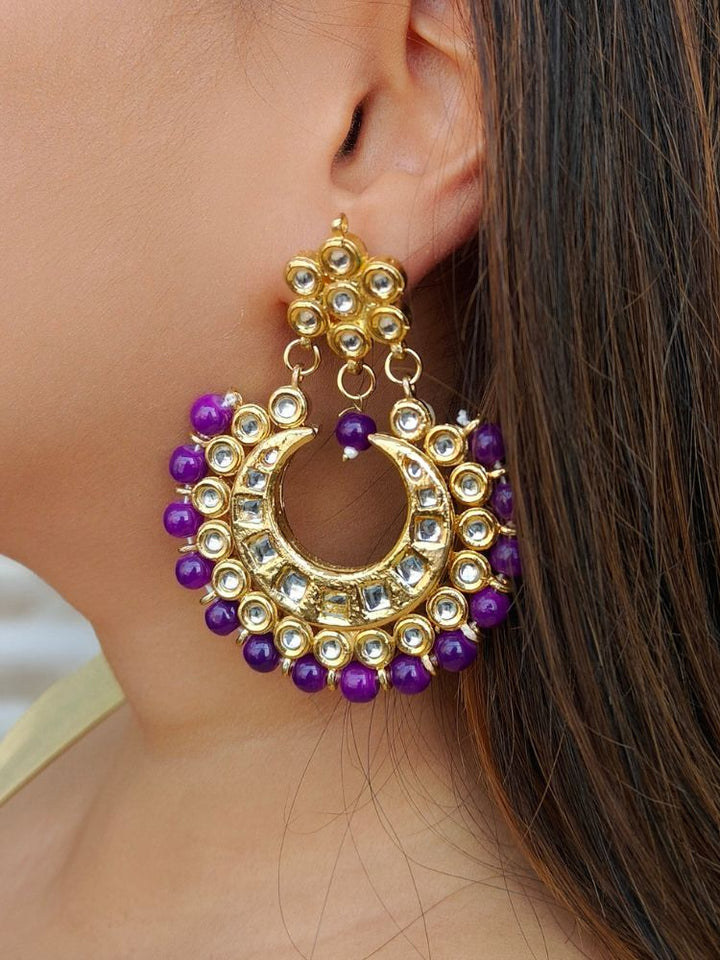 A close-up of a womans ear wearing Natalia Purple Earrings—crescent moon-shaped chandbali, gold-toned Kundan stones and purple beads—ideal for Mehendi functions or as wedding ceremony accessories.