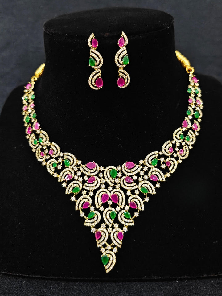 Close-up of an ornate Indo-Western Ruby Pink & Green Diamond gold Collar jewellery set and earrings with American Diamond and Ruby Pink & Green Colored Stones. Close-up of a cocktail party look featuring a premium American diamond necklace. Mehendi function outfit styled with a lightweight American Diamond necklace.