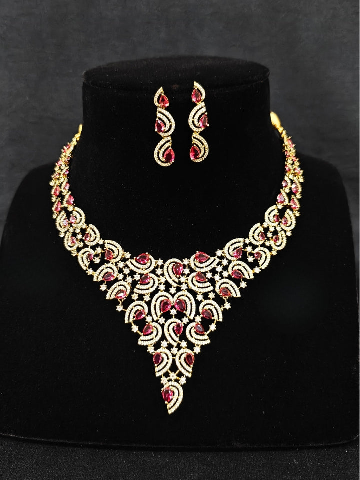 Close-up of an ornate Indo-Western Red Diamond gold Collar jewellery set and earrings with American Diamond and Red Colored Stones. Close-up of a cocktail party look featuring a premium American diamond necklace. Mehendi function outfit styled with a lightweight American Diamond necklace.