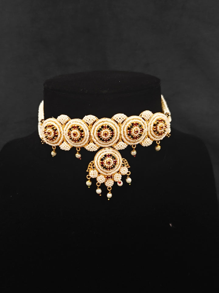 Close-up of an ornate traditional (Bright Gold Polish) Red,Green and White Choker jewellery set and earrings and Ring with Pearls and Red & Green Colored Stones. Mehendi ceremony look completed with a handcrafted Pearl jewelry set. Woman wearing a vibrant Pearl artificial jewelry set for celebrations.