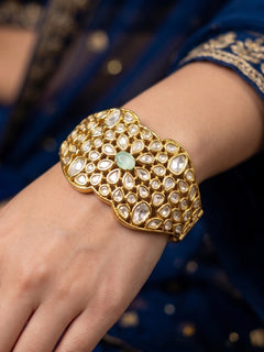 Close-up of a woman wearing an ornate traditional (Gold Polish) White Bracelet with Polki and Mint Green Colored Stone in Middle. Woman stacking artificial Polki Bracelet for a festive Diwali celebration. Close-up of an anti-tarnish artificial Polki bracelet styled for wedding guests.