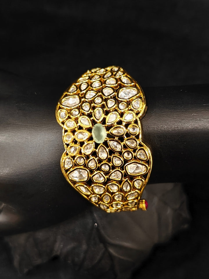 Close-up of an ornate traditional (Gold Polish) White Bracelet with Polki and Mint Green Colored Stone in Middle. Woman stacking artificial Polki Bracelet for a festive Diwali celebration. Close-up of an anti-tarnish artificial Polki bracelet styled for wedding guests.