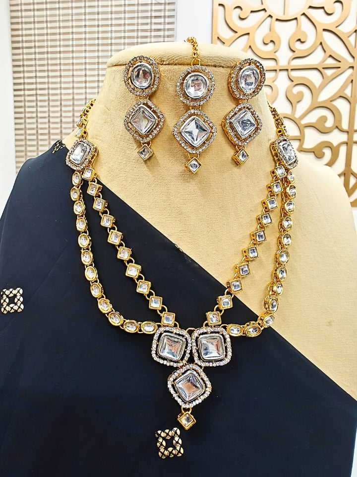 The Nitya Necklace Set features gold and white Kundan, with two layered necklace and matching oversized earrings along with a maantikka —displayed on a mannequin in a black saree, its the perfect accent for your wedding ceremony dress.