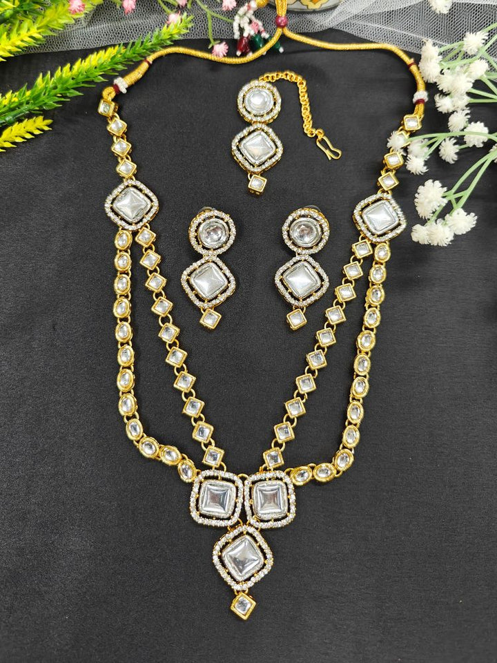 The Nitya Necklace Set features gold and white Kundan, with two layered necklace and matching oversized earrings along with a maantikka —displayed on a black Surface, its the perfect accent for your wedding ceremony dress.