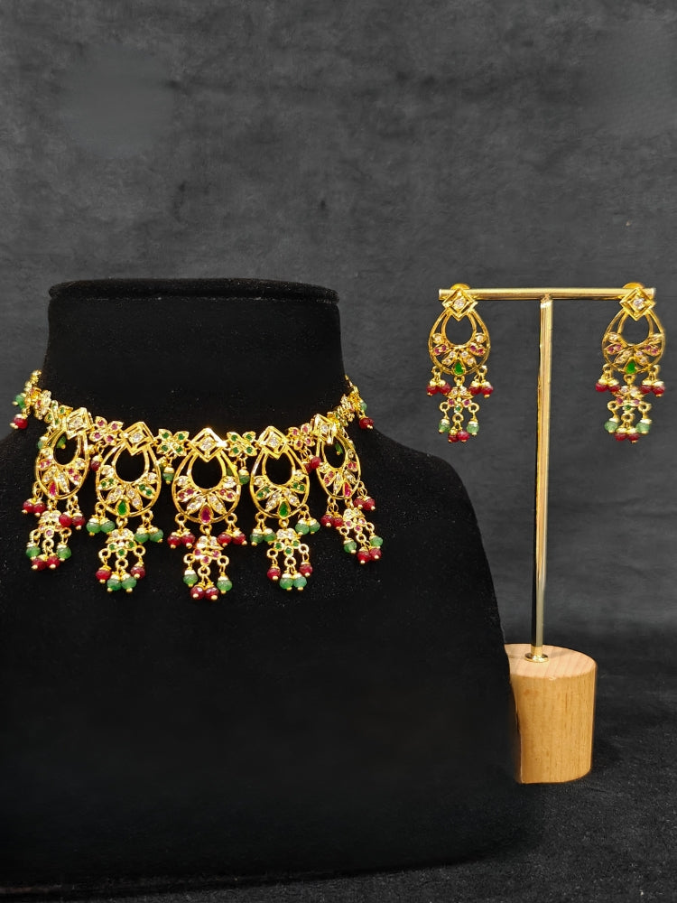 Close-up of an ornate traditional jadau gold jewellery set and jadau earrings with pearls and Ruby Pink & Green gemstones. Elegant  look featuring a luxury Jadau artificial jewelry set. Festive celebration look featuring a Jadau artificial necklace.