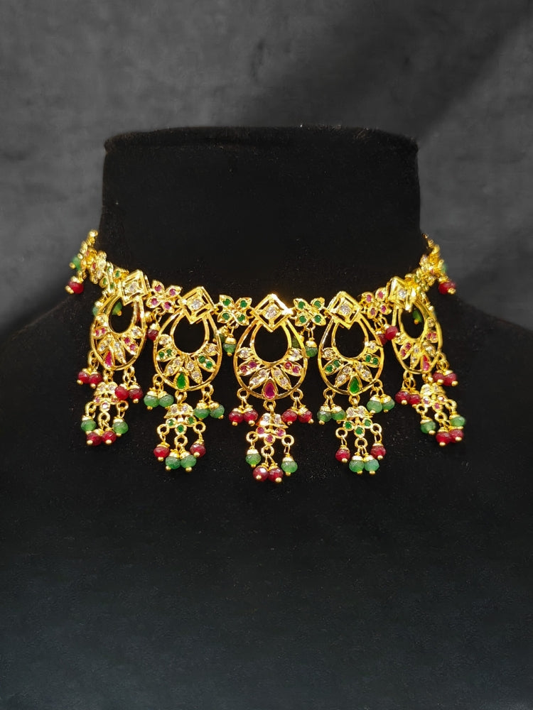 Close-up of an ornate traditional jadau gold jewellery set and jadau earrings with pearls and Ruby Pink & Green gemstones. Elegant  look featuring a luxury Jadau artificial jewelry set. Festive celebration look featuring a Jadau artificial necklace.