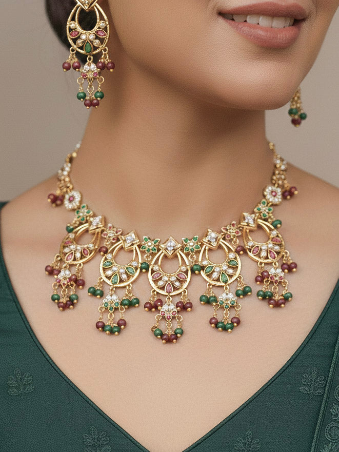 Close-up of a woman wearing an ornate traditional jadau gold jewellery set and jadau earrings with pearls and Ruby Pink & Green gemstones. Elegant  look featuring a luxury Jadau artificial jewelry set. Festive celebration look featuring a Jadau artificial necklace.