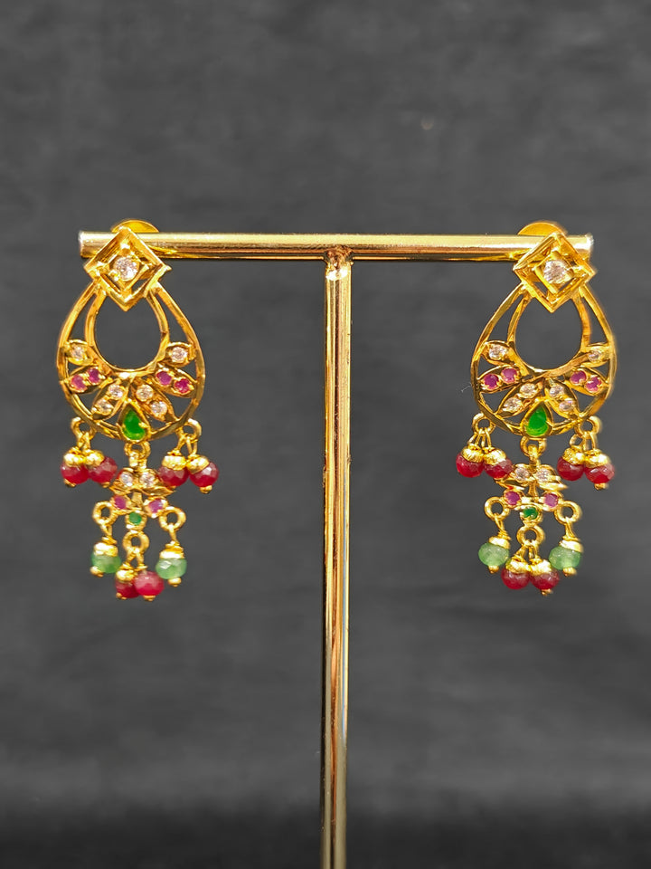 Close-up of an ornate traditional jadau gold jewellery set and jadau earrings with pearls and Ruby Pink & Green gemstones. Elegant  look featuring a luxury Jadau artificial jewelry set. Festive celebration look featuring a Jadau artificial necklace.