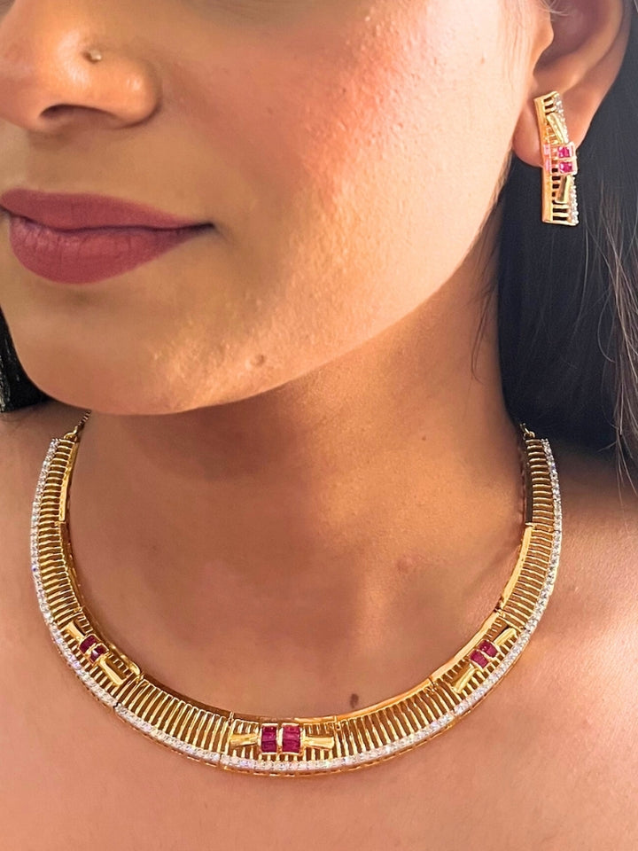 A woman wears the Noctelle Pink Necklace Set—gold with red and white diamond stones in a geometric design. The American Diamonds jewelry beautifully complements her warm skin tone and natural makeup.