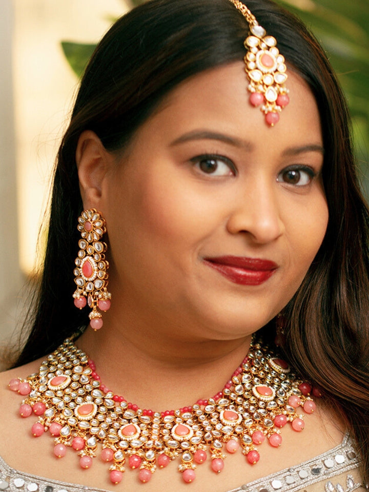 Close-up of a woman wearing an ornate traditional Pink Collar jewellery set and earrings and maangtikka with Kundan, Beads and Pearls. Royal bridal look featuring a traditional Kundan necklace set. Woman wearing trending Kundan artificial jewelry for wedding season in India. Close-up of intricate Kundan craftsmanship in artificial bridal jewelry.