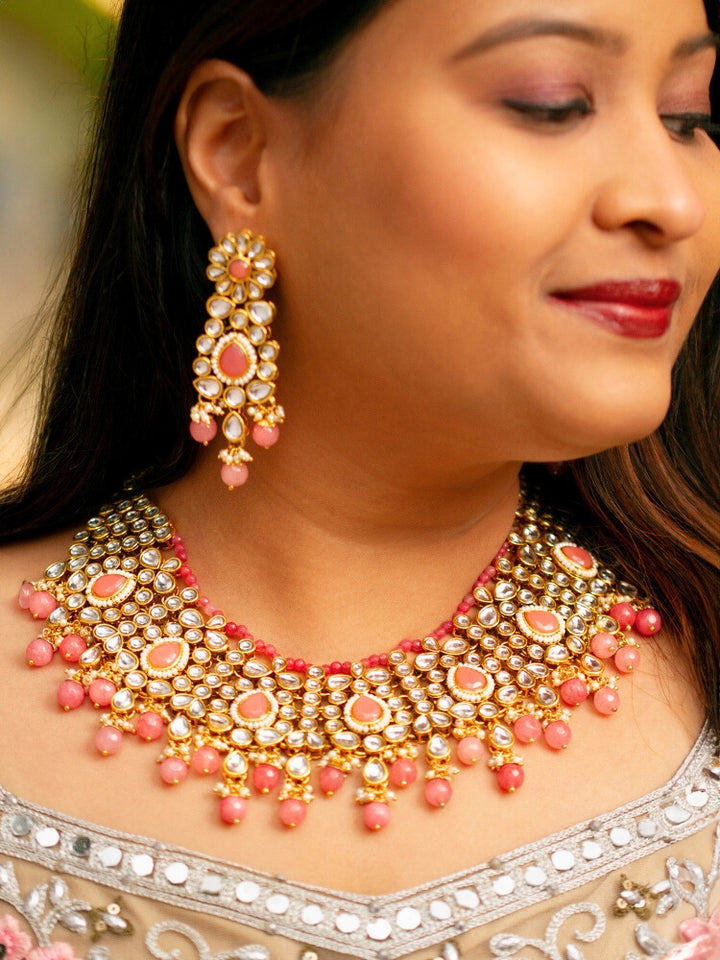 Close-up of a woman wearing an ornate traditional Pink Collar jewellery set and earrings and maangtikka with Kundan, Beads and Pearls. Royal bridal look featuring a traditional Kundan necklace set. Woman wearing trending Kundan artificial jewelry for wedding season in India. Close-up of intricate Kundan craftsmanship in artificial bridal jewelry.