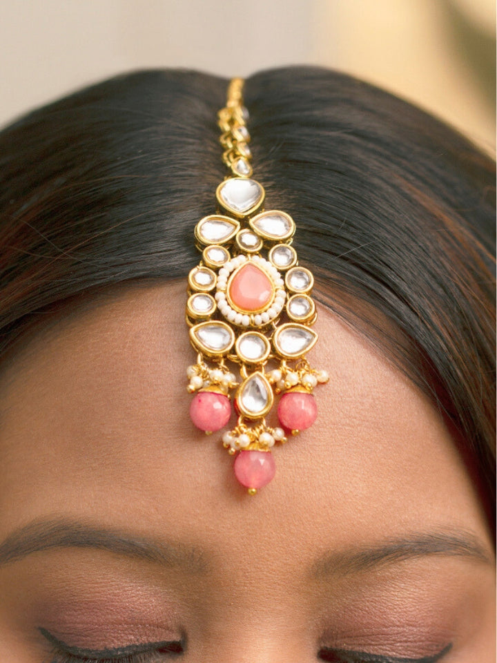 Close-up of a woman wearing an ornate traditional Pink Collar jewellery set and earrings and maangtikka with Kundan, Beads and Pearls. Royal bridal look featuring a traditional Kundan necklace set. Woman wearing trending Kundan artificial jewelry for wedding season in India. Close-up of intricate Kundan craftsmanship in artificial bridal jewelry.