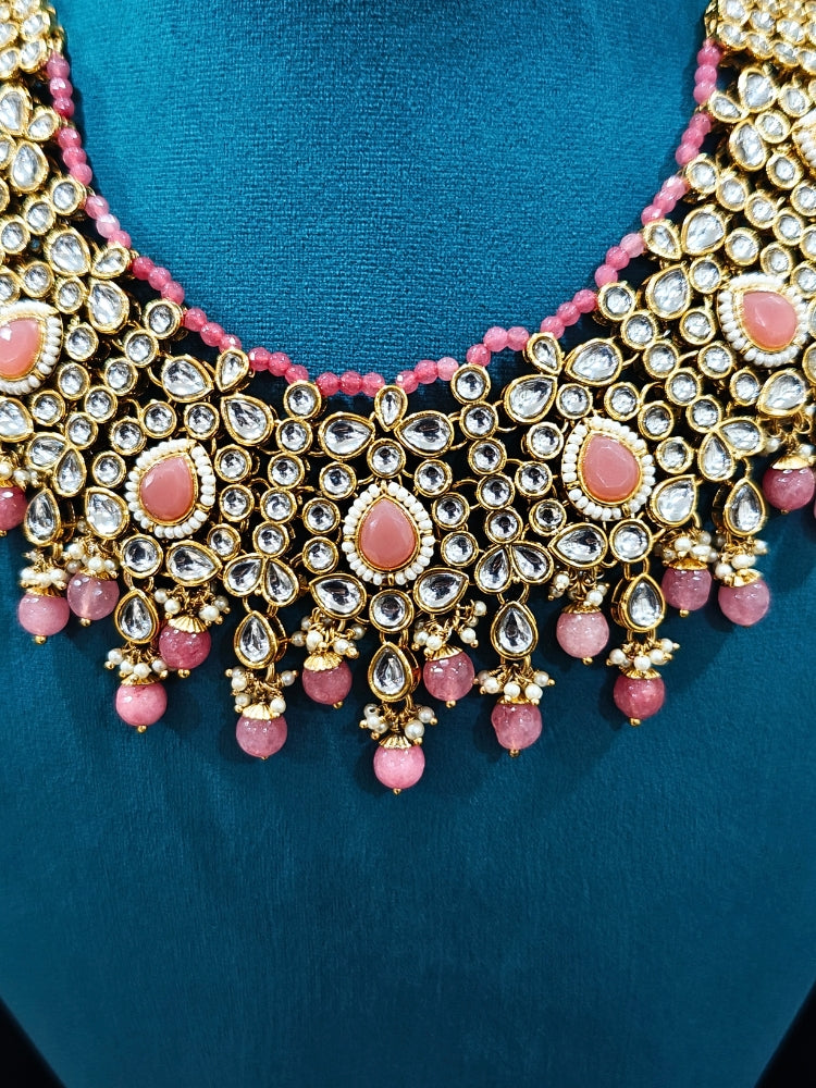 Close-up of an ornate traditional Pink Collar jewellery set and earrings and maangtikka with Kundan, Beads and Pearls. Royal bridal look featuring a traditional Kundan necklace set. A trending Kundan artificial jewelry for wedding season in India. Close-up of intricate Kundan craftsmanship in artificial bridal jewelry.