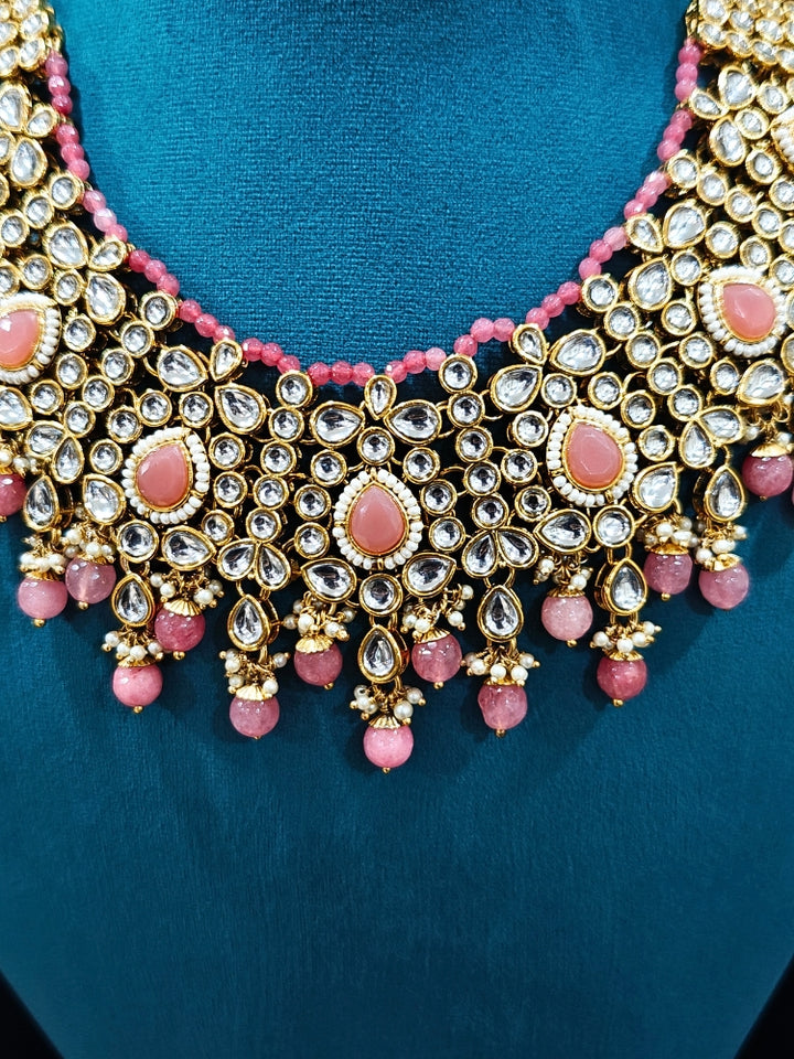 Close-up of an ornate traditional Pink Collar jewellery set and earrings and maangtikka with Kundan, Beads and Pearls. Royal bridal look featuring a traditional Kundan necklace set. A trending Kundan artificial jewelry for wedding season in India. Close-up of intricate Kundan craftsmanship in artificial bridal jewelry.