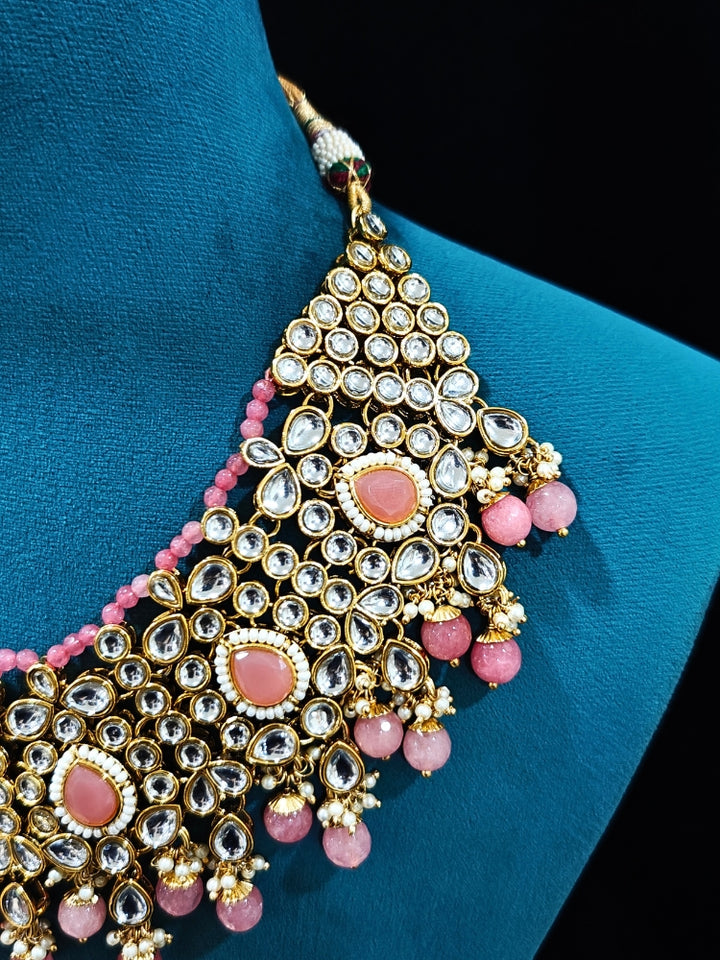 Close-up of an ornate traditional Pink Collar jewellery set and earrings and maangtikka with Kundan, Beads and Pearls. Royal bridal look featuring a traditional Kundan necklace set. A trending Kundan artificial jewelry for wedding season in India. Close-up of intricate Kundan craftsmanship in artificial bridal jewelry.