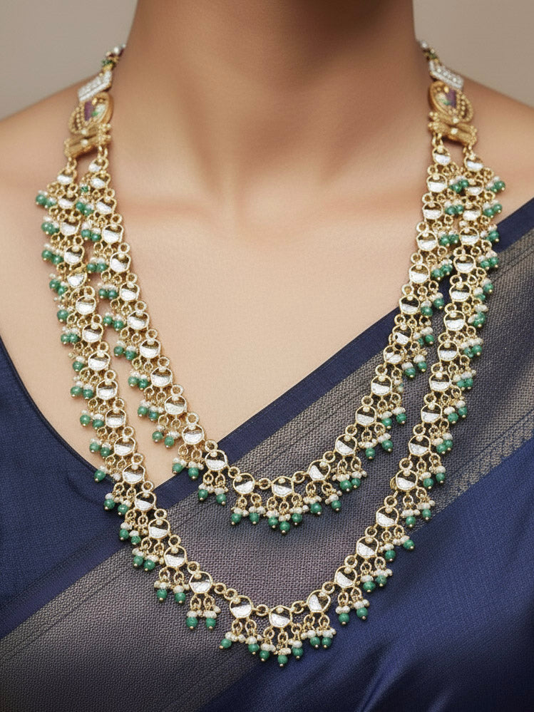 Close-up of a woman wearing an ornate traditional Mint Pink and Green Heritage gold Long Layered jewellery set and earrings with Colored Stones and Beads. Festive celebration outfit paired with a handcrafted heritage jewelry set. Festive  outfit styled with a royal heritage necklace. Festive celebration look enhanced with traditional Meenakari jewelry.