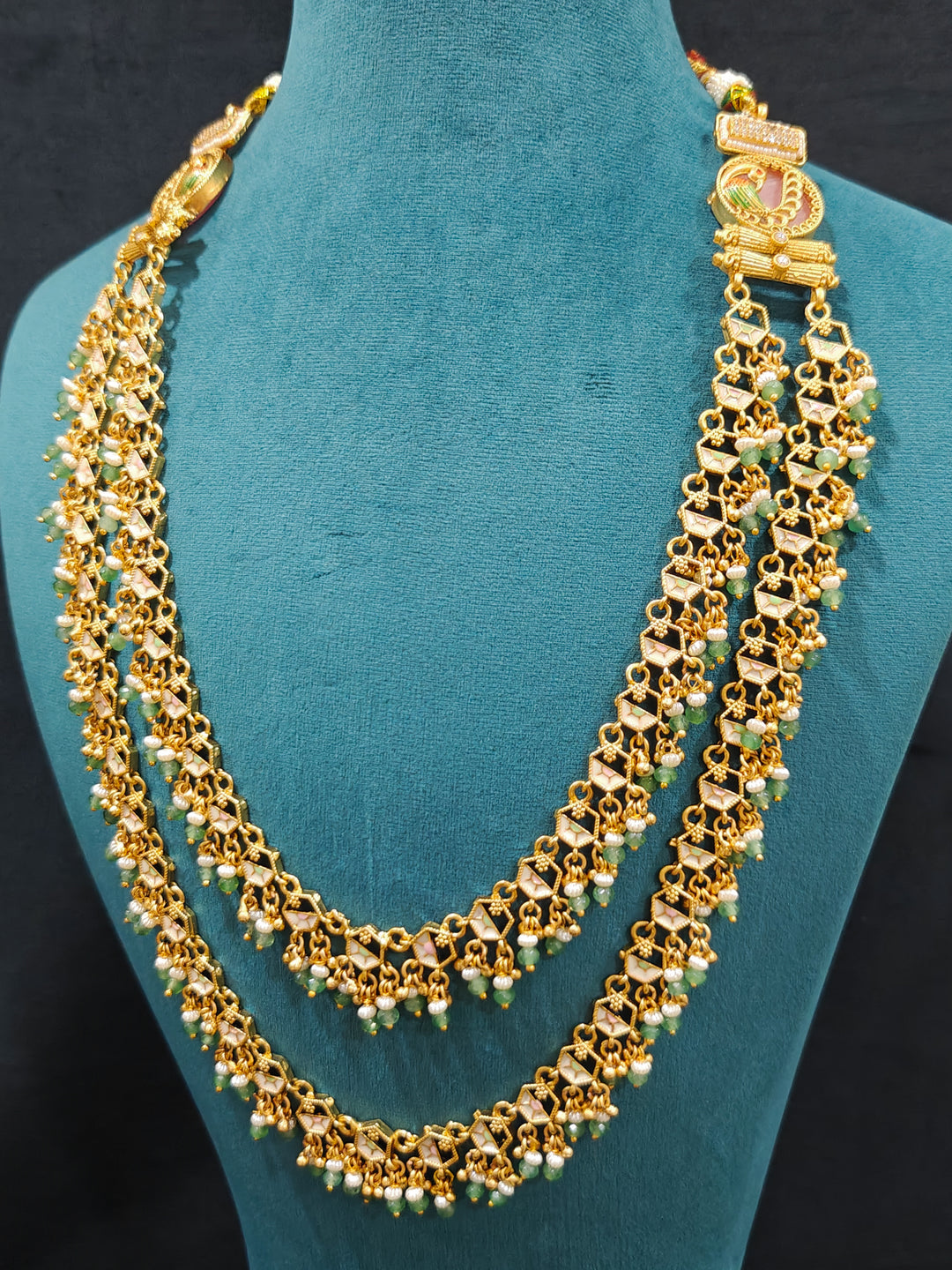 Close-up of an ornate traditional Mint Pink and Green Heritage gold Long Layered jewellery set and earrings with Colored Stones and Beads. Festive celebration outfit paired with a handcrafted heritage jewelry set. Festive  outfit styled with a royal heritage necklace. Festive celebration look enhanced with traditional Meenakari jewelry.