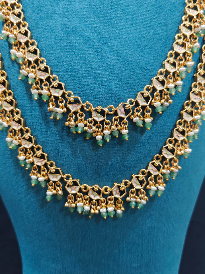 Close-up of an ornate traditional Mint Pink and Green Heritage gold Long Layered jewellery set and earrings with Colored Stones and Beads. Festive celebration outfit paired with a handcrafted heritage jewelry set. Festive  outfit styled with a royal heritage necklace. Festive celebration look enhanced with traditional Meenakari jewelry.