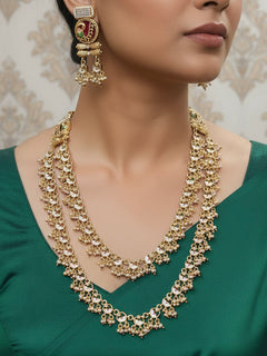 Close-up of a woman wearing an ornate traditional Dark Pink Rajwadi gold Long Layered jewellery set and earrings with Colored Stones and Beads. Festive celebration outfit paired with a handcrafted heritage jewelry set. Festive  outfit styled with a royal heritage necklace.
