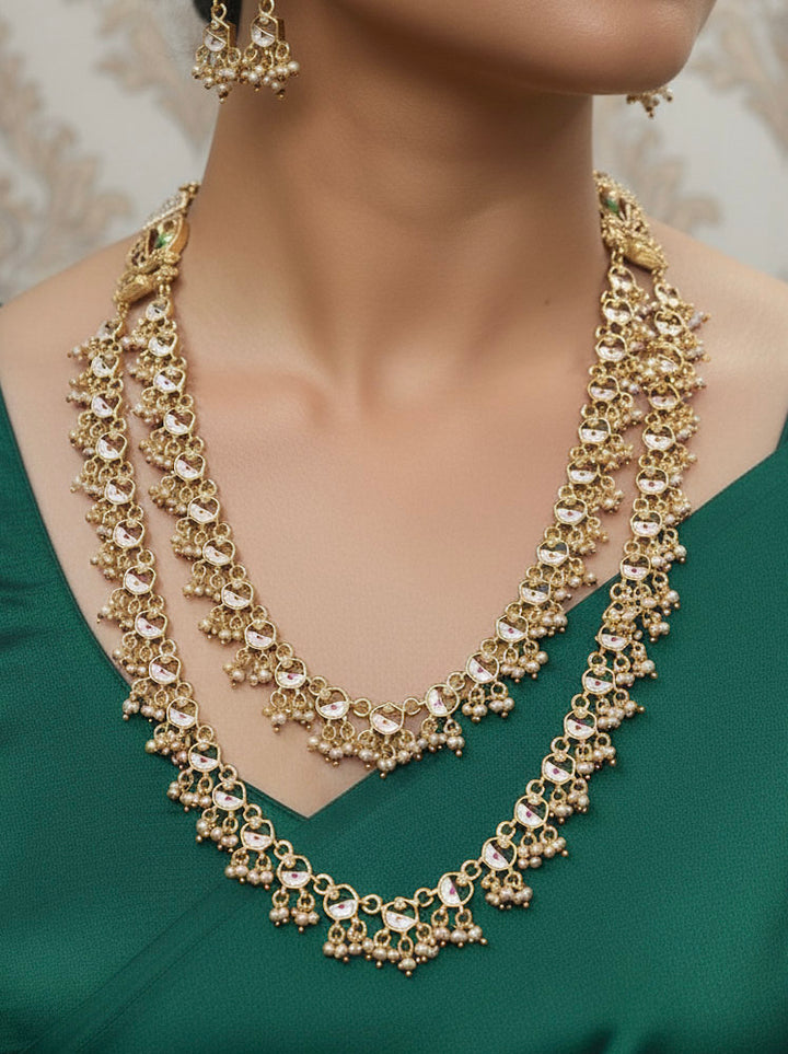 Close-up of a woman wearing an ornate traditional Dark Pink Heritage gold Long Layered jewellery set and earrings with Colored Stones and Beads. Festive celebration outfit paired with a handcrafted heritage jewelry set. Festive  outfit styled with a royal heritage necklace.