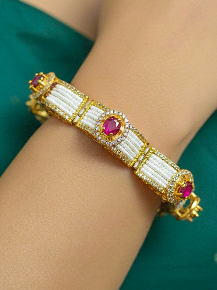 Close-up of a woman wearing an ornate Traditional Diamond Bracelet with Gold Polish, Pink Colored Stones, American Diamond, Pearls and filigree Work. Reception-ready look featuring a statement American diamond Bracelet. Close-up of a cocktail party look featuring a premium American diamond Bracelet.