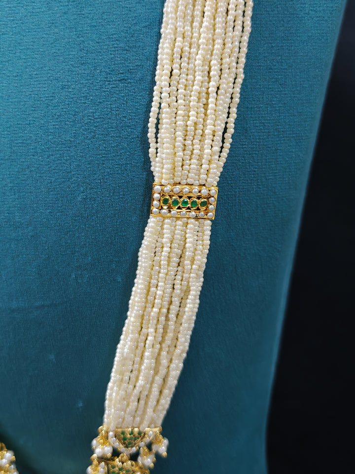 Pearl necklace with a gold clasp with green jadau stones on a blue background .a royal Jadau necklace for festive events in India and traditional Indian wedding. elegant green Jadau long necklace, adorned with delicate pearls and intricate detailing, adds a royal charm to any traditional look.

