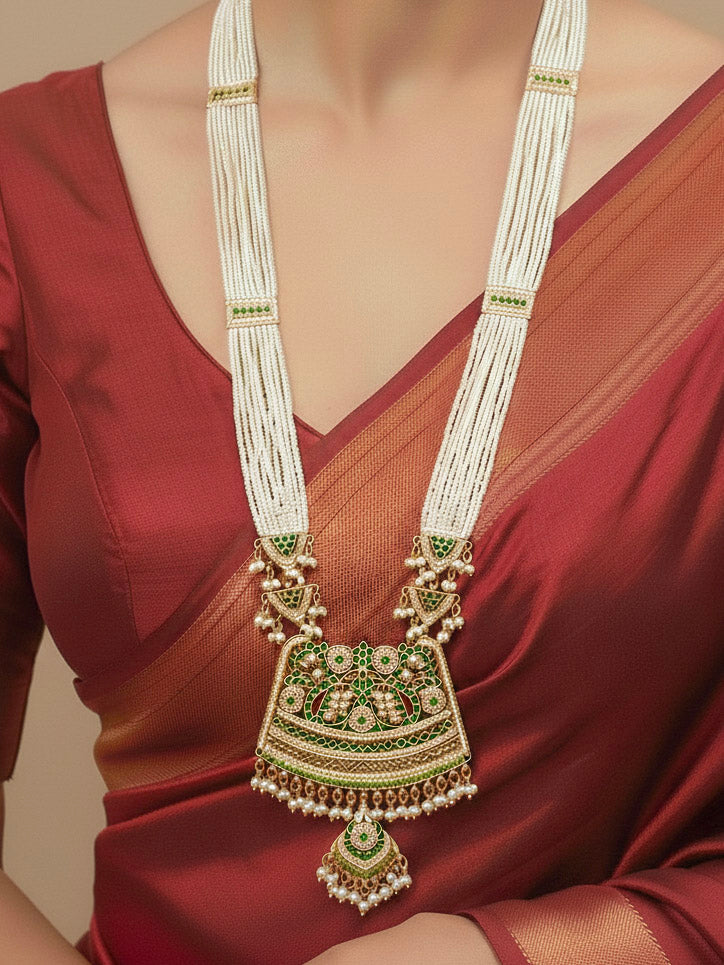 Close-up of a woman wearing a gold Indian traditional long jadau jewellery with pearls and jadau green stones, and matching jadau earrings. This authentic jadau jewelry set can we worn as jadau necklace set for weddings. 
