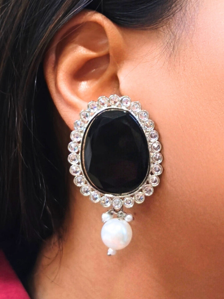 A close-up of a womans ear wearing Pamela Black Earrings, which feature an oval shaped Black colored stone,  American Diamond border and a dangling white pearl-perfect for pairing with your wedding ceremony dress.