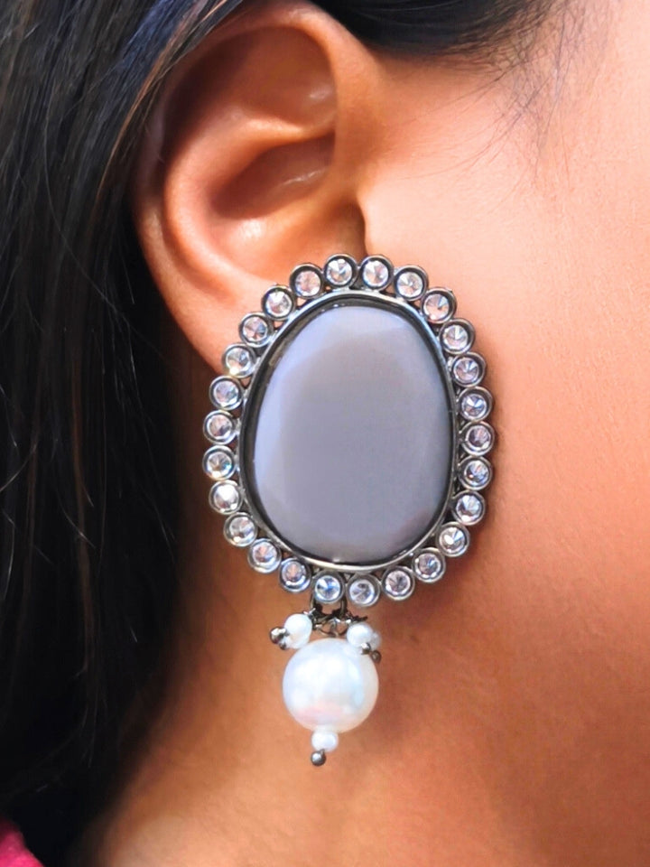 A close-up of a womans ear wearing Pamela Grey Earrings, which feature an oval shaped Grey colored stone,  American Diamond border and a dangling white pearl-perfect for pairing with your wedding ceremony dress.