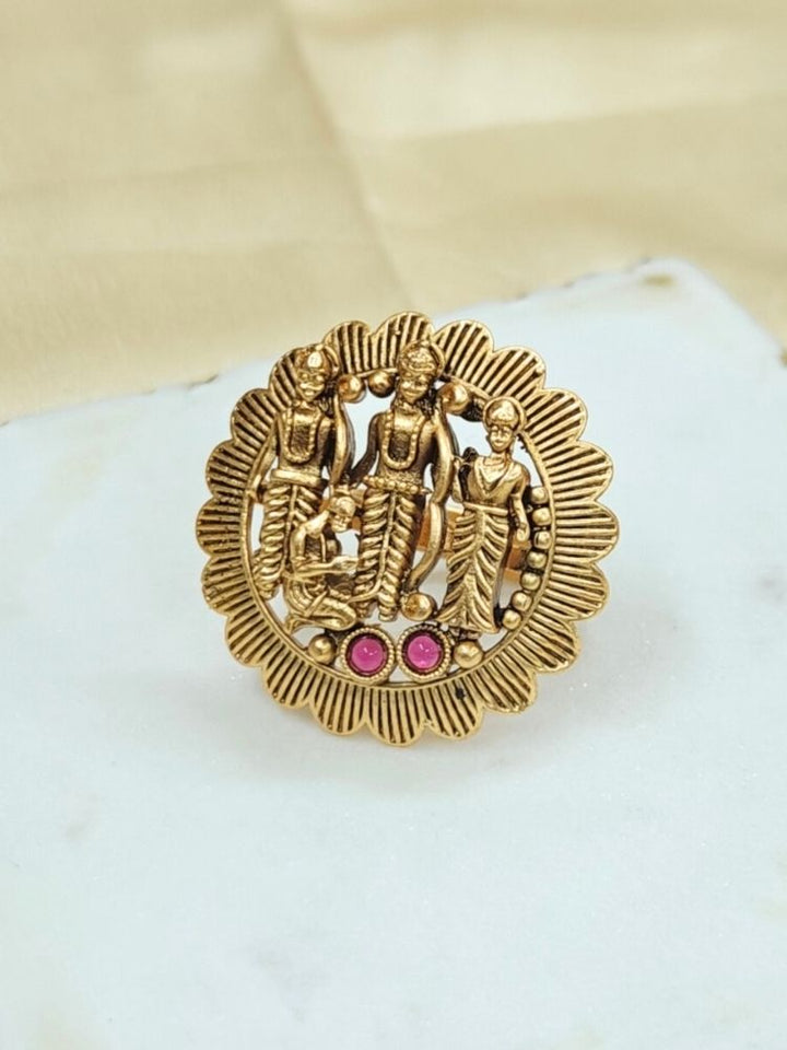 The Pavan Putra Red Ring features a round gold design with intricate carvings of Ram, Laxman and Sitaji, accented by three pink stones—an exquisite ethnic accessory, ideal for wedding and religious ceremonies.
