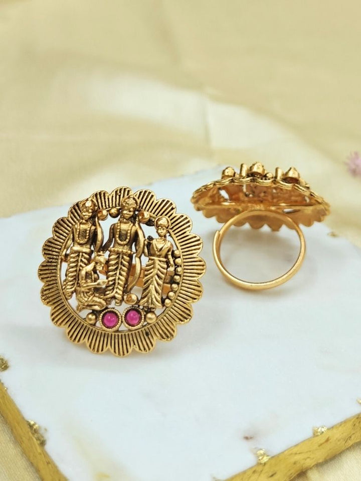 The Pavan Putra Red Ring features a round gold design with intricate carvings of Ram, Laxman and Sitaji, accented by three pink stones—an exquisite ethnic accessory, ideal for wedding and religious ceremonies.
