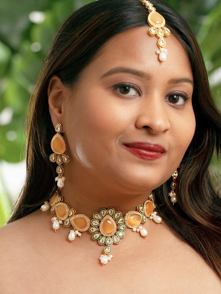 Close-up of a women wearing an ornate traditional Peach Choker jewellery set and earrings and maangtikka with Kundan, Monalisa Stone, American Diamonds, Beads and Reverse American Diamonds and tumble stones. A graceful woman wearing a trending Colored Stone necklace for a 2026 wedding celebration. Elegant wedding jewelry look featuring a premium artificial Colored Stone necklace.