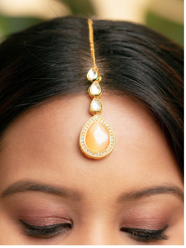 Close-up of a woman wearing an ornate traditional (Gold Polish) Peach Collar jewellery set and earrings and maangtikka with Kundan and American Diamonds. Woman wearing trending Kundan artificial jewelry for wedding season in India. Bride wearing a royal Kundan artificial necklace for wedding rituals.
