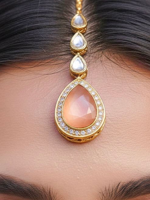 Close-up of a woman wearing an ornate traditional (Gold Polish) Peach Collar jewellery set and earrings and maangtikka with Kundan and American Diamonds. Woman wearing trending Kundan artificial jewelry for wedding season in India. Bride wearing a royal Kundan artificial necklace for wedding rituals.